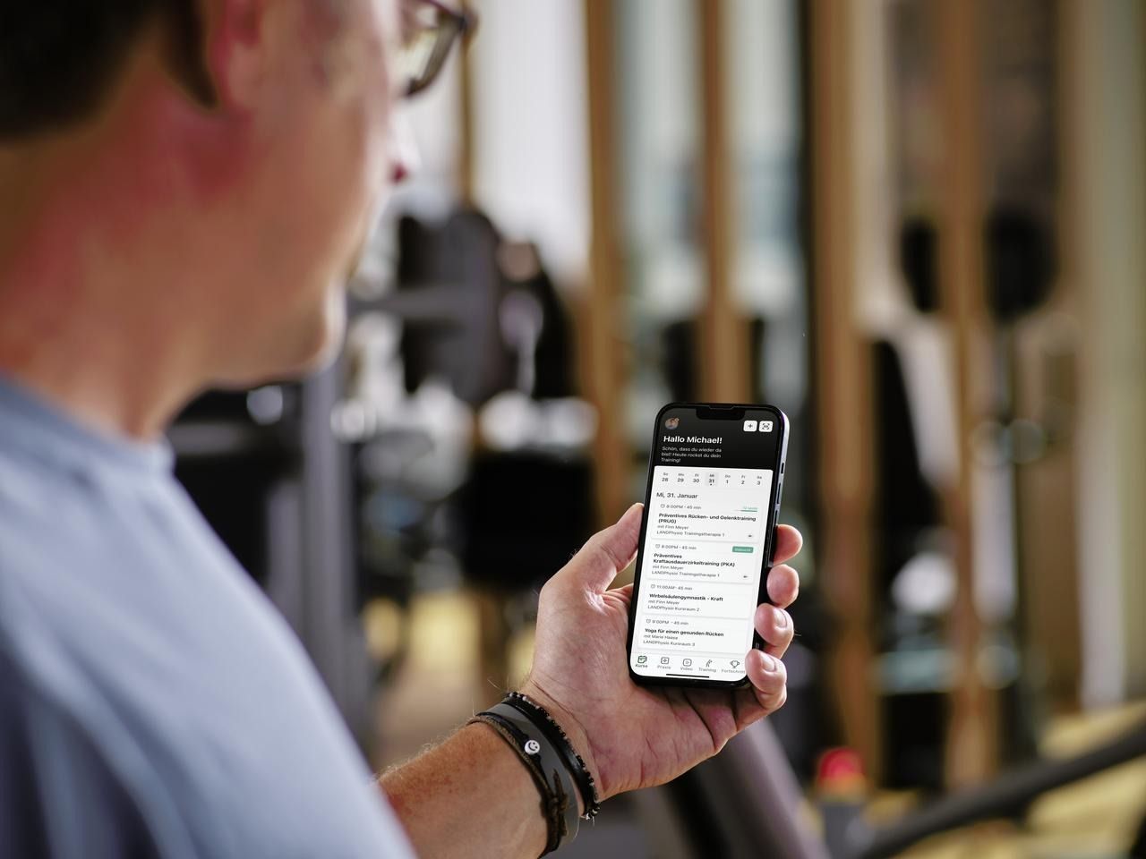 Ein Mann hält in einem Fitnessstudio ein Mobiltelefon in der Hand.