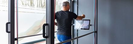 Ein Mann steht in einem Türrahmen und hält ein Tablet in der Hand.