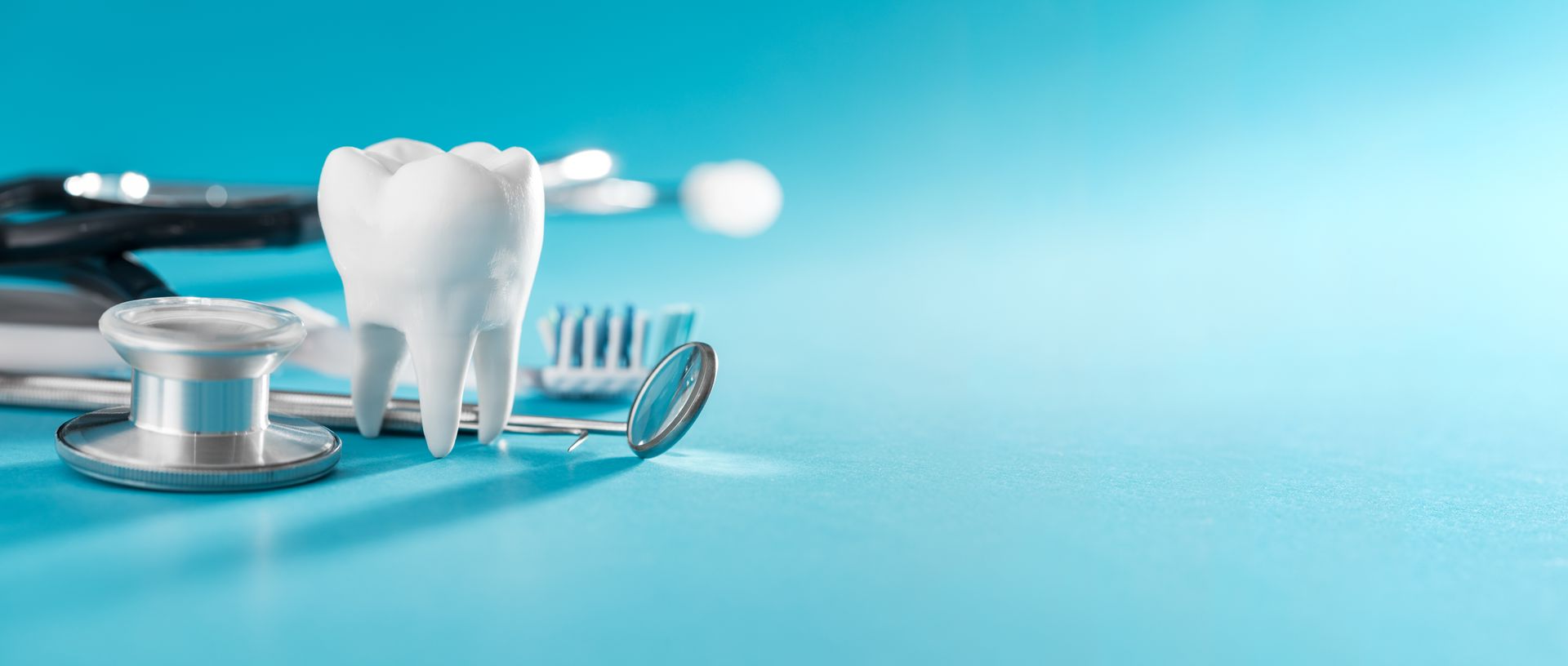 Zahnförmiger Behälter mit zahnärztlichen Instrumenten in einer Zahnarztpraxis; im Hintergrund ist ein blauer Stuhl zu sehen.