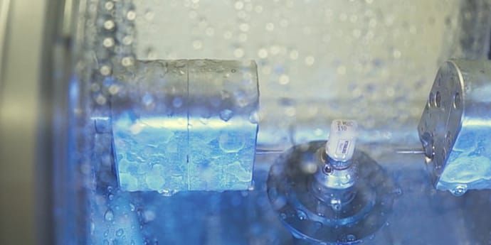 Nahaufnahme einer in Betrieb befindlichen zahnärztlichen Fräsmaschine, die Wasser versprüht, bläulich schimmernder Innenraum.