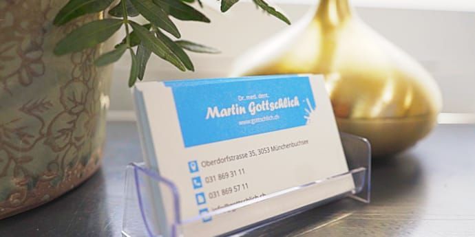 Visitenkarte im Halter mit blau-weißem Muster, neben einer Vase und einer Pflanze.