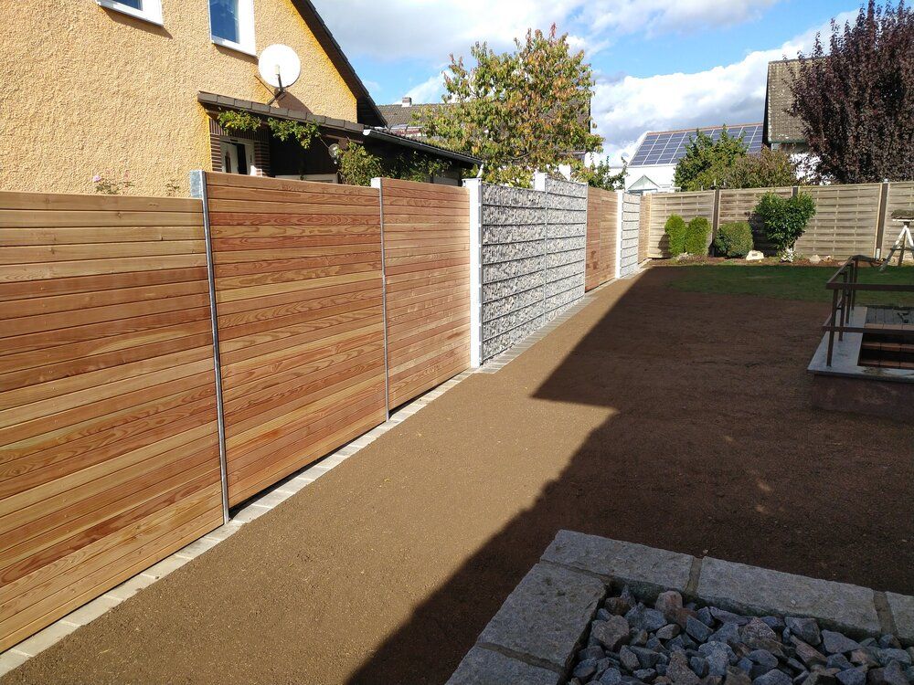 Ein Zaun aus Holz und Stein umgibt den Hinterhof, der mit einem braunen Kiesweg und grünem Rasen bewachsen ist.