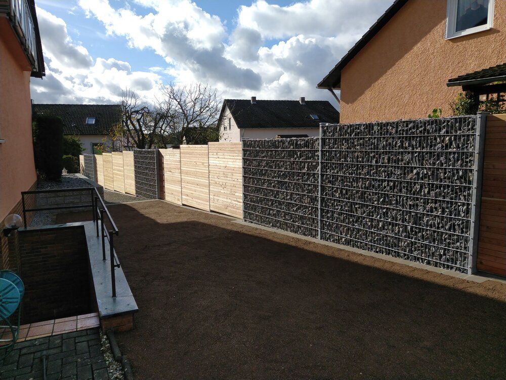 Sichtschutzzaun aus Stein und Holz zwischen den Häusern an einem sonnigen Tag.