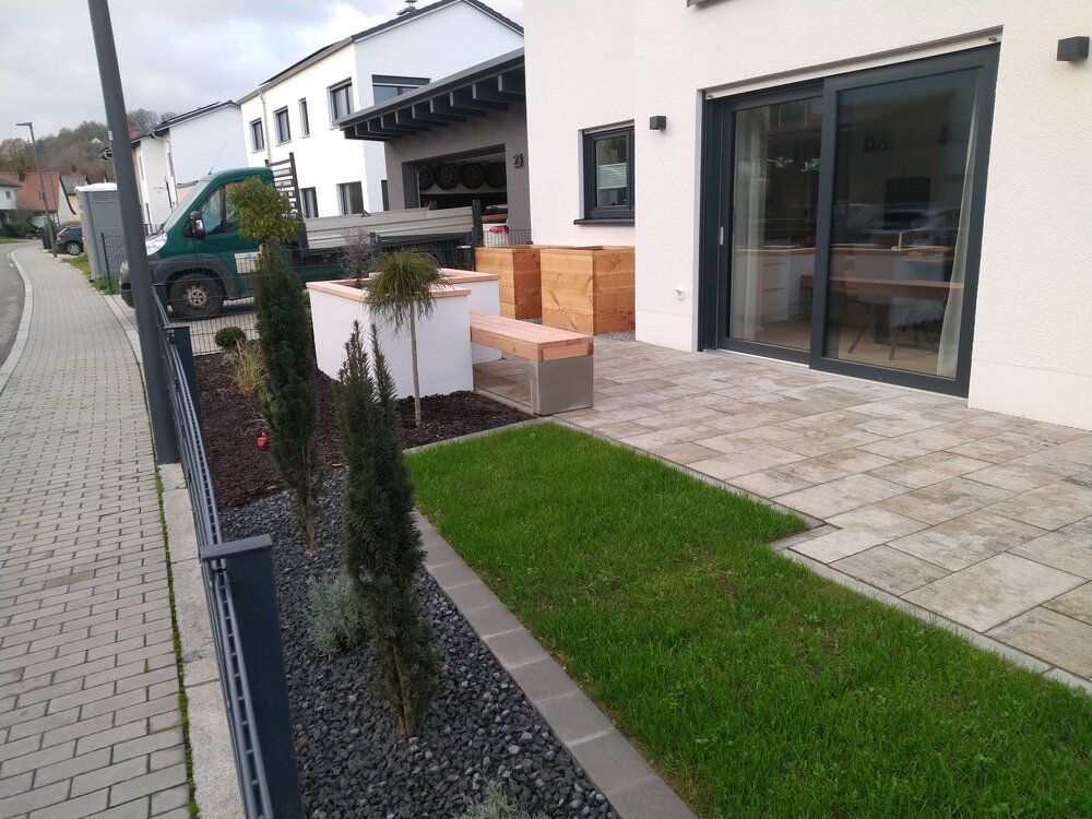 Modernes Hausäußeres mit Terrasse, kleinem Rasen, Gartengestaltung und Gehweg.