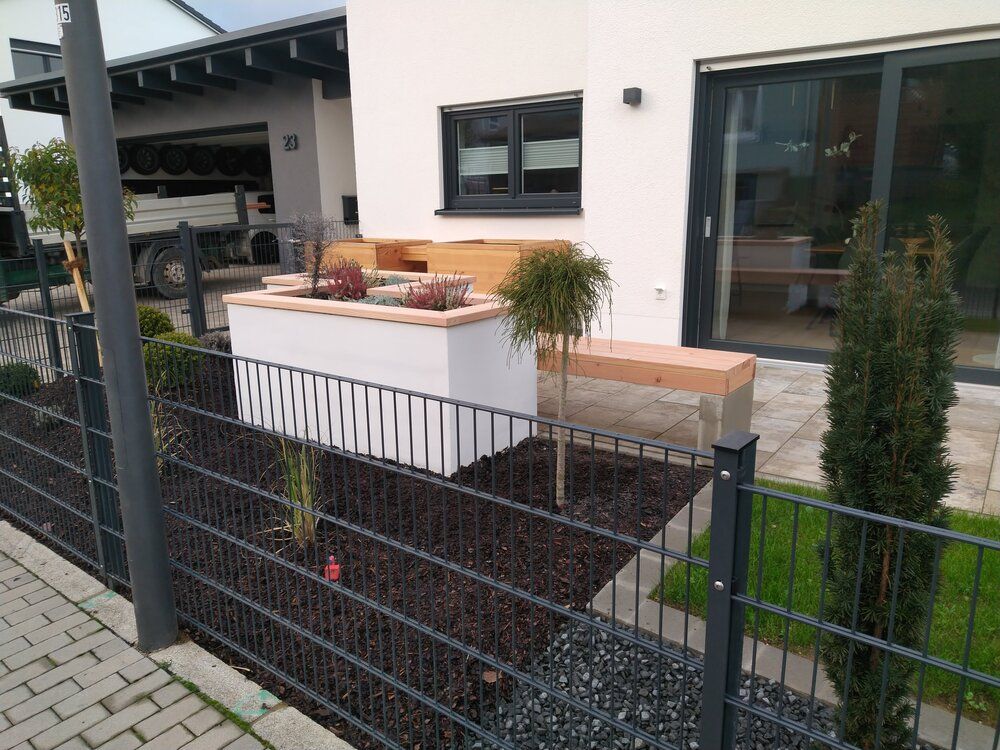 Modernes Hausäußeres mit schwarzem Zaun, Hochbeet und Holzbank.