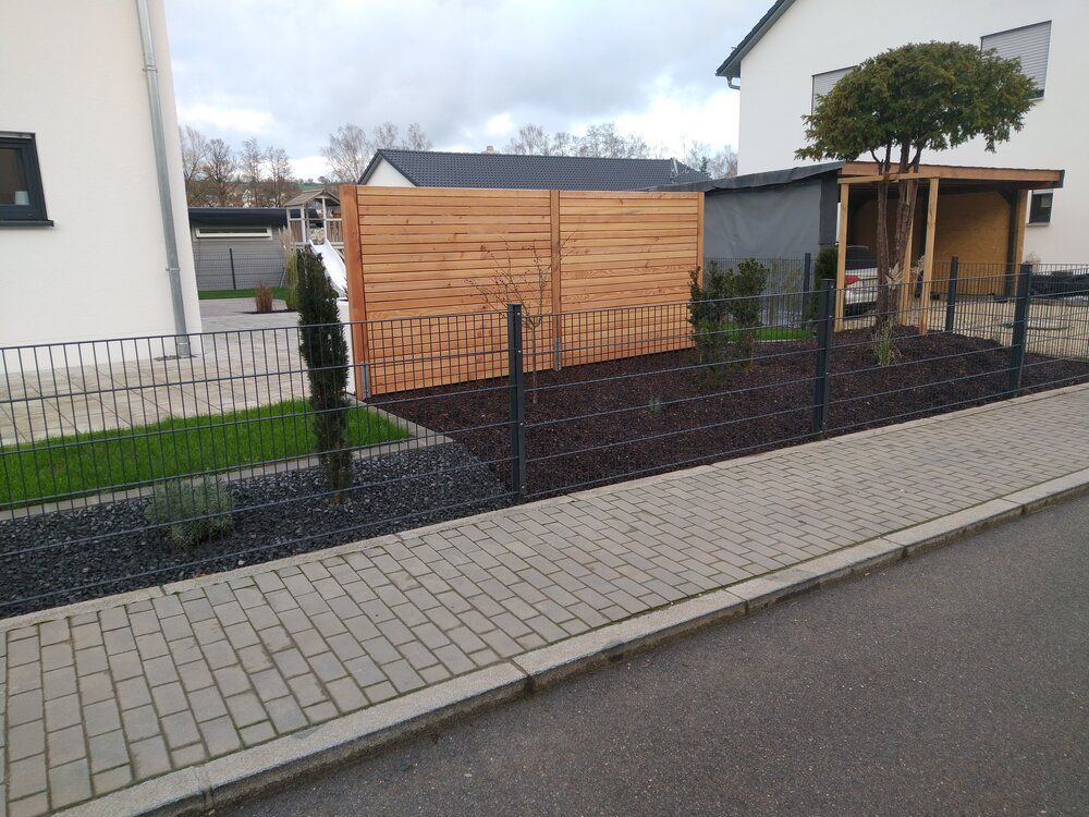 Ein Vorgarten mit angelegtem Garten, Holzzaun, dunklem Mulch und einem Haus an einem bewölkten Tag.