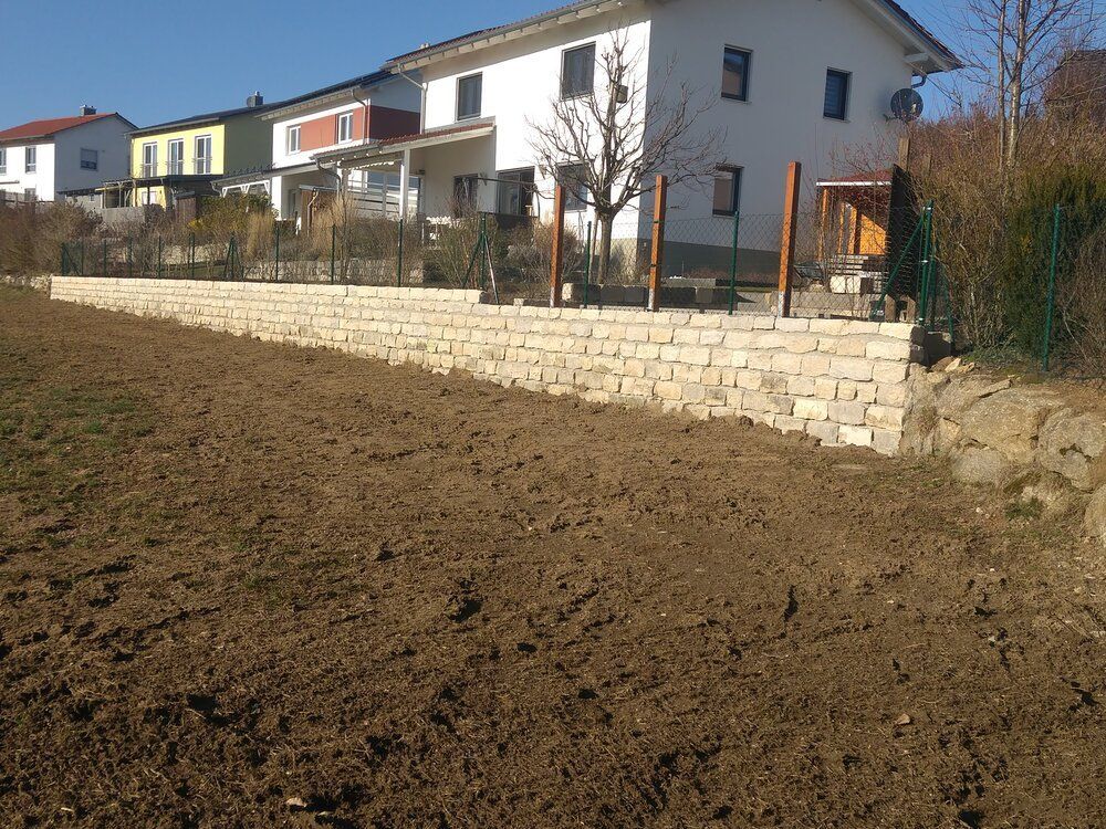 Ein vorbereitetes Feld mit einer steinernen Stützmauer vor den Häusern an einem sonnigen Tag.