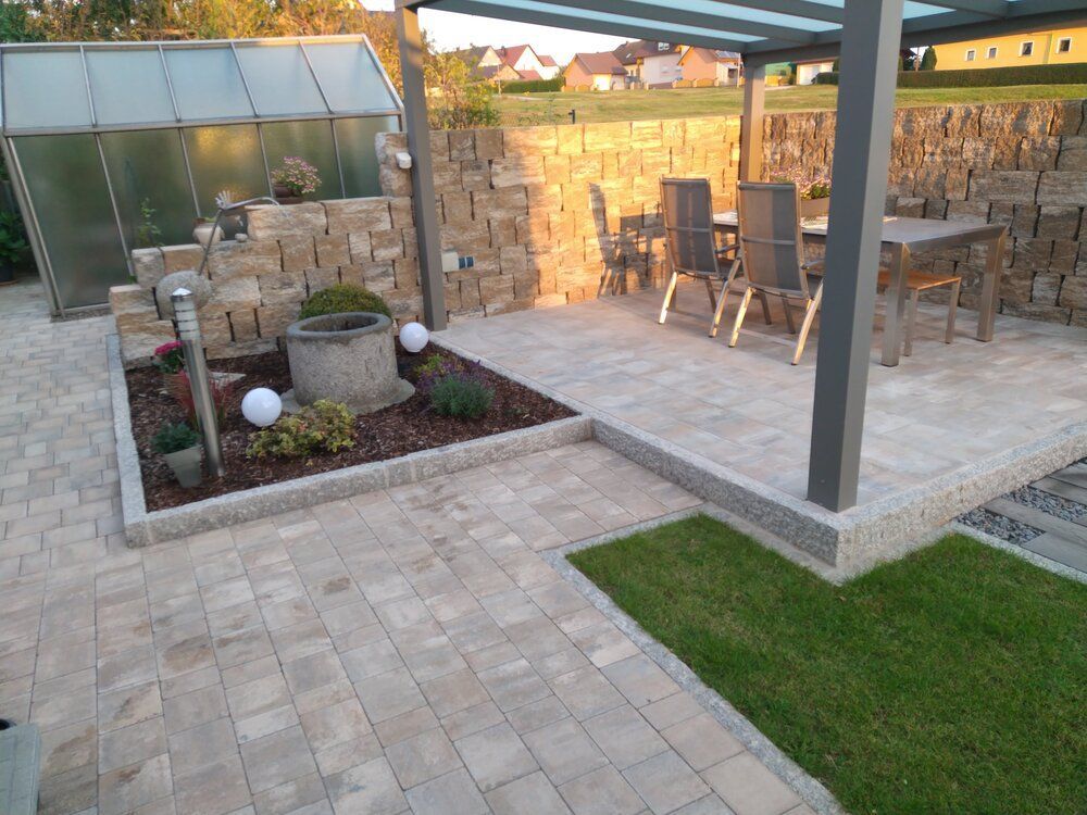 Steinterrasse mit Esstisch, Steinmauer und kleiner Rasenfläche.