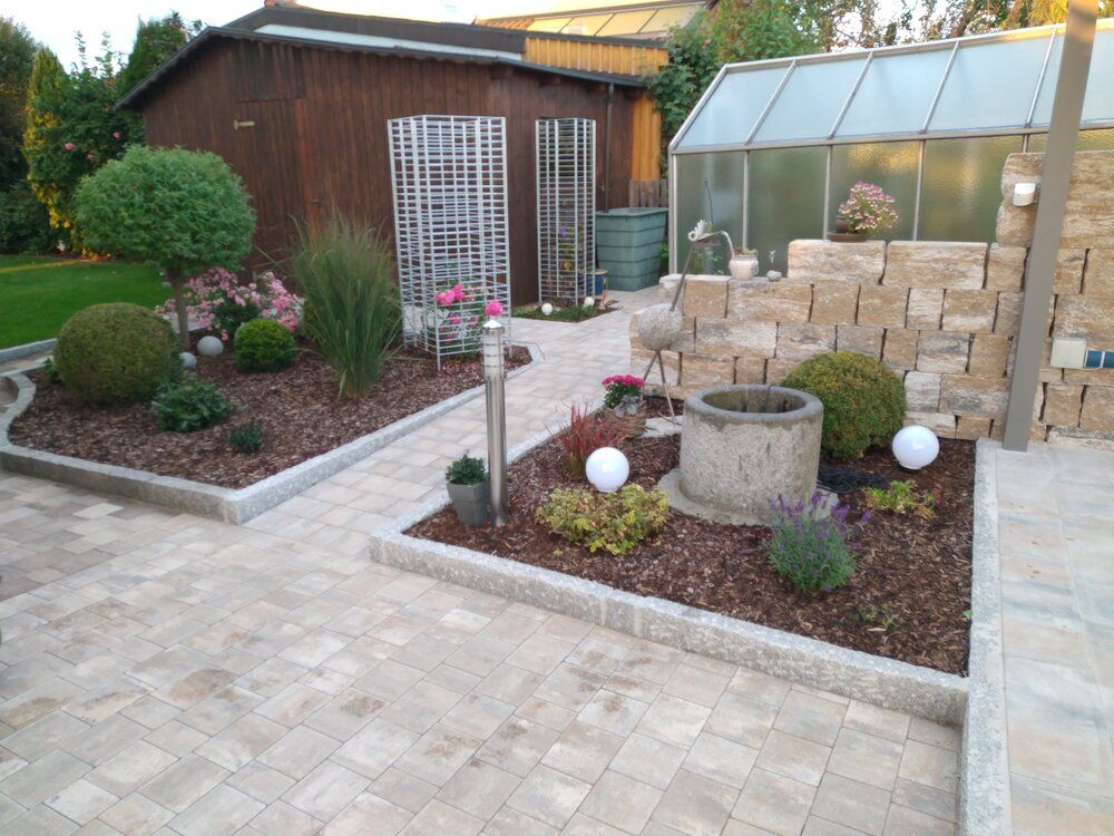 Gut gestalteter Garten mit Steinweg, Blumenbeeten, Sträuchern und einem Gewächshaus.