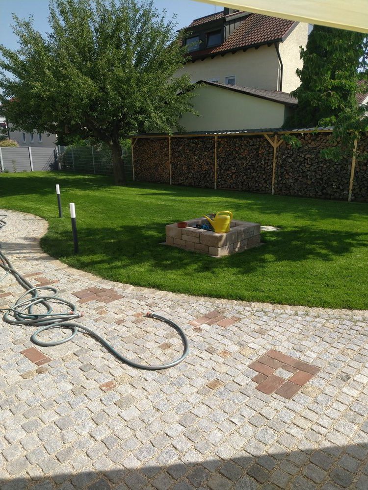 Ein gepflegter Hinterhof mit Steinterrasse, Rasenfläche, Feuerstelle, Brennholzlager und einem Haus im Hintergrund.