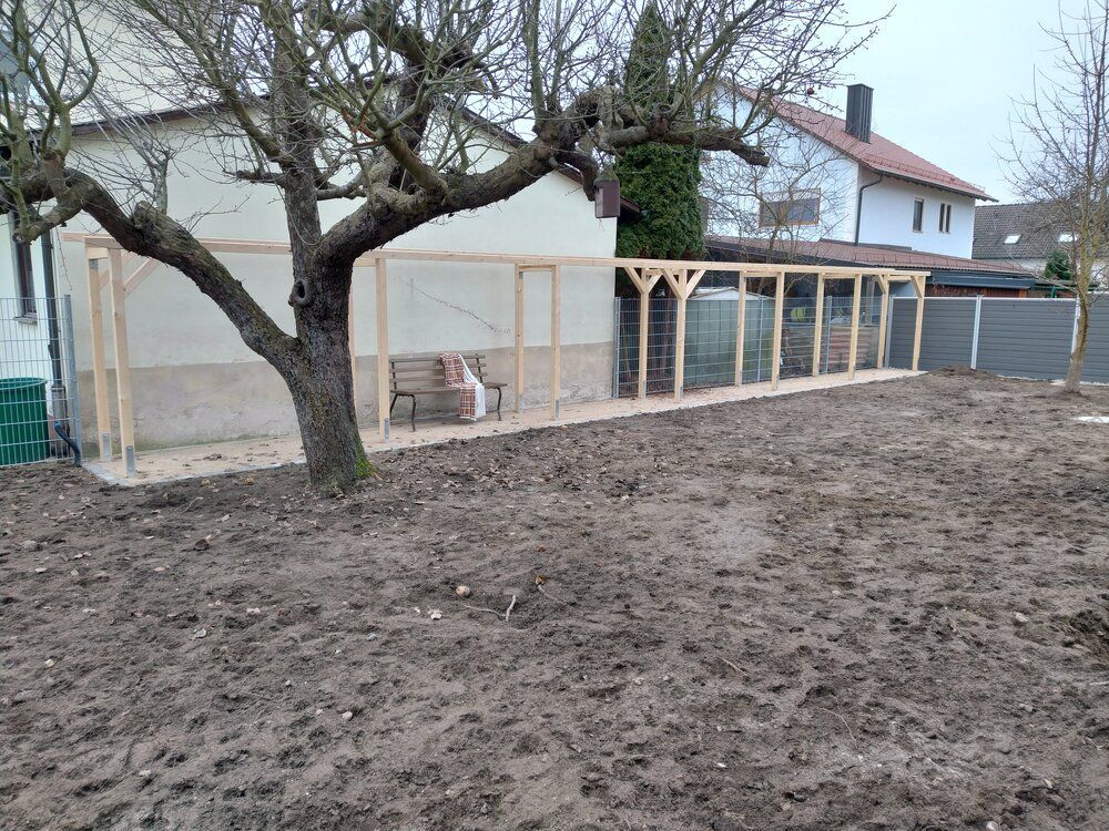 Ein langes, hölzernes Katzengehege verläuft entlang eines Hauses, davor befindet sich ein matschiger Hof.