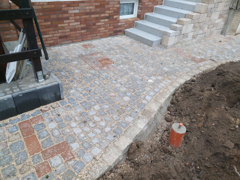 Ein Weg aus Ziegeln und Kopfsteinpflaster führt zu den Stufen und zum Hauseingang.