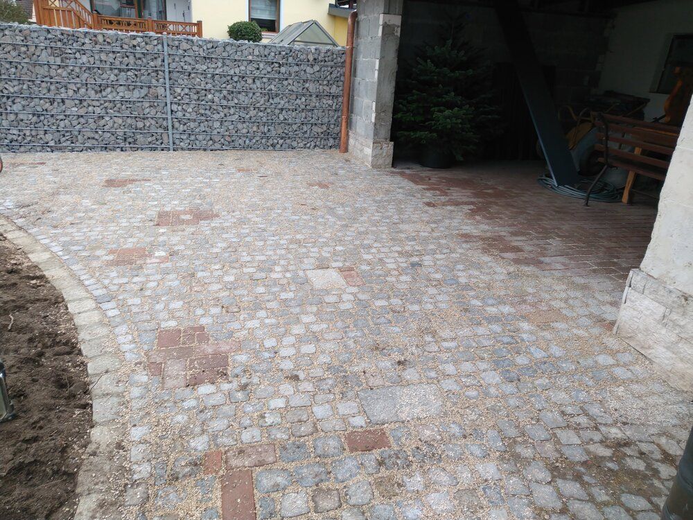 Kopfsteinpflasterauffahrt mit Steinmauer auf der linken Seite, die zu einer Garageneinfahrt führt.