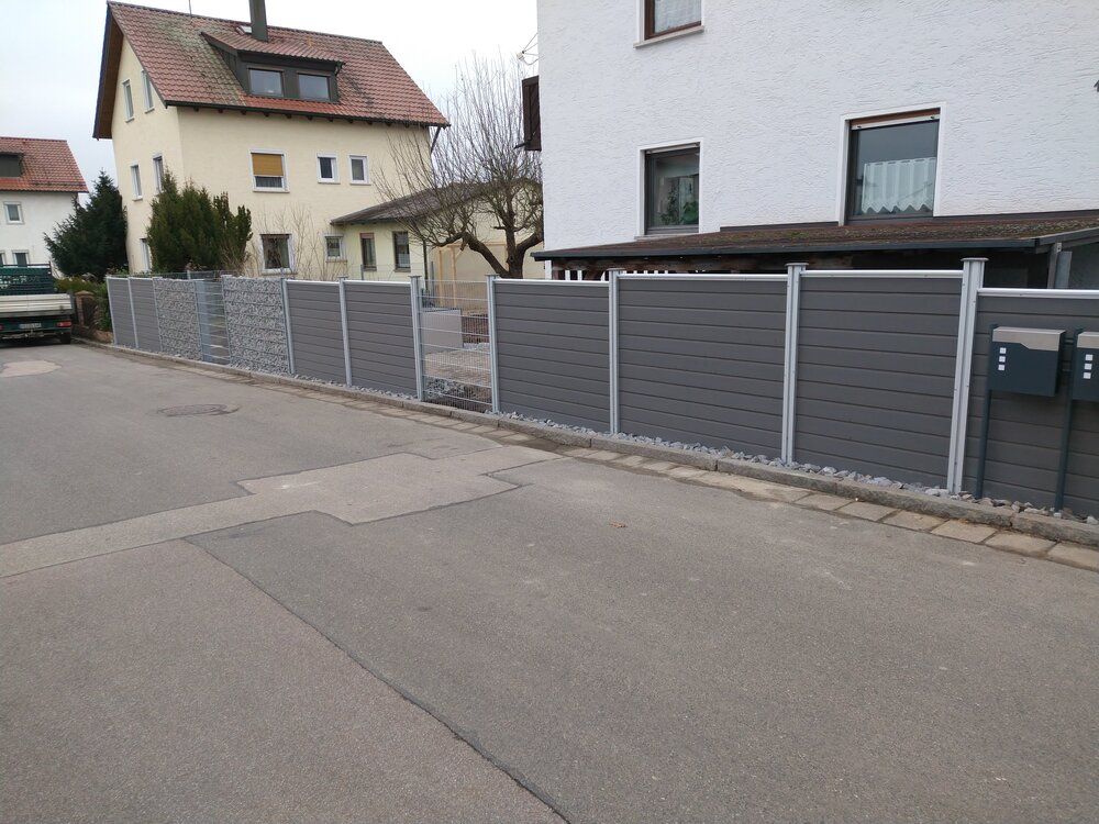 Graue und steinerne Mauer entlang einer Straße vor den Häusern.