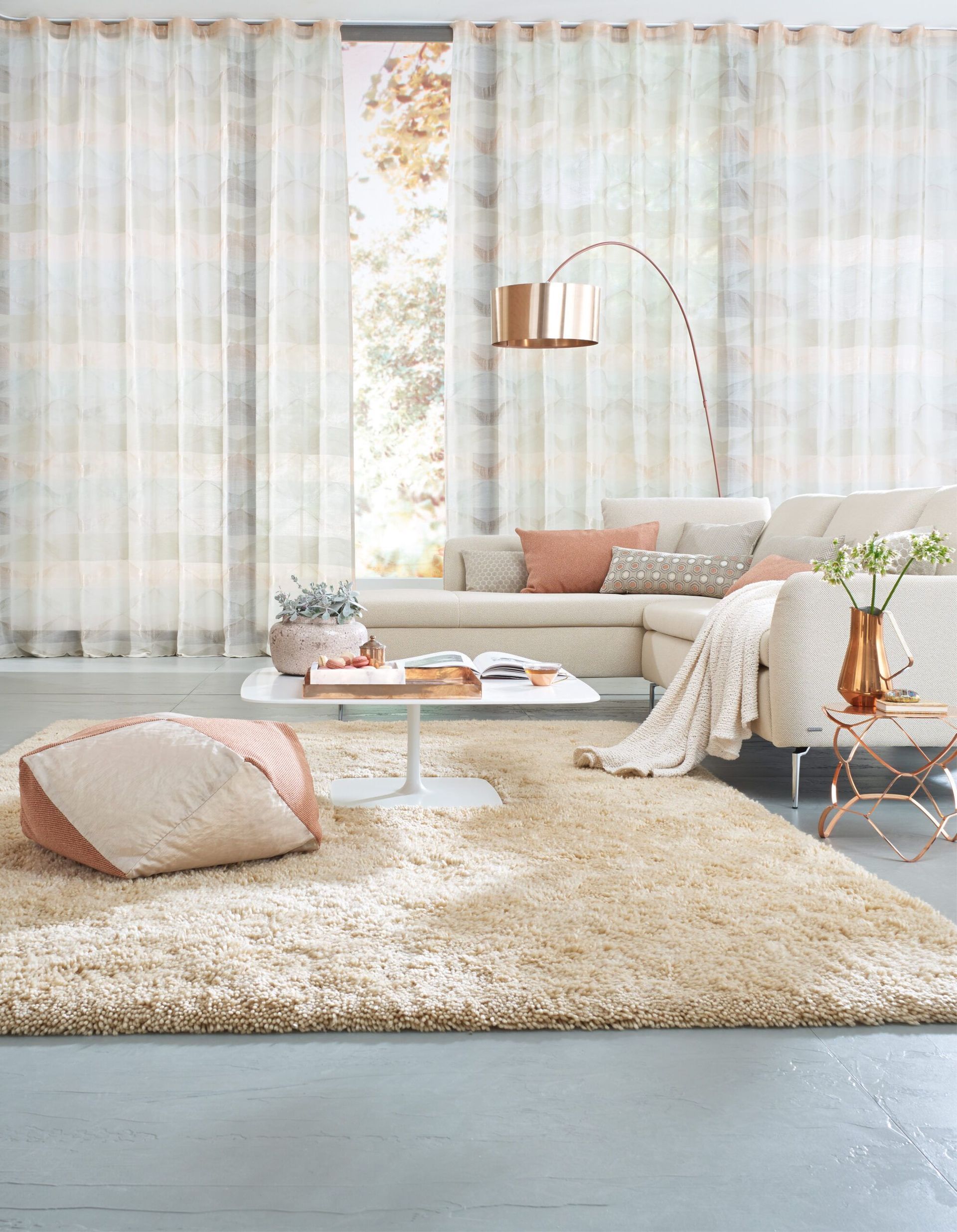 Wohnzimmer mit beigefarbenem Shaggy-Teppich, weißem Sofa, transparenten Vorhängen und goldenen Akzenten.