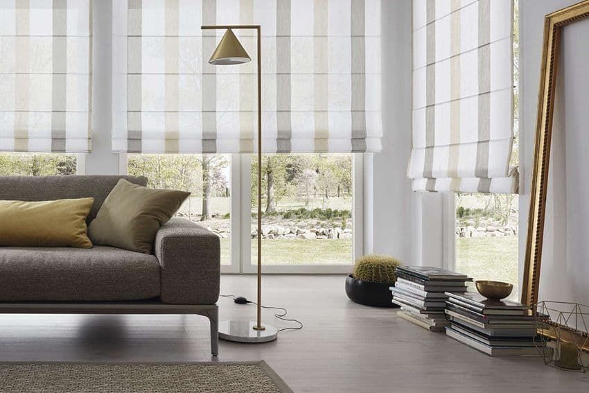 Wohnzimmer mit gestreiften Fensterrollos, Sofa mit Kissen, Stehlampe und einem großen Spiegel.