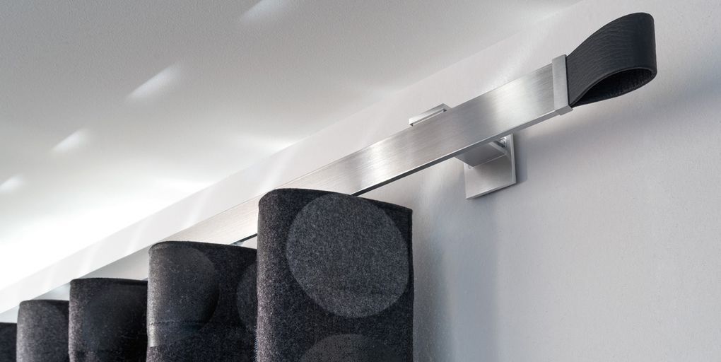 Nahaufnahme einer modernen Gardinenstange mit gemusterten Vorhängen. Grau- und Silbertöne dominieren.