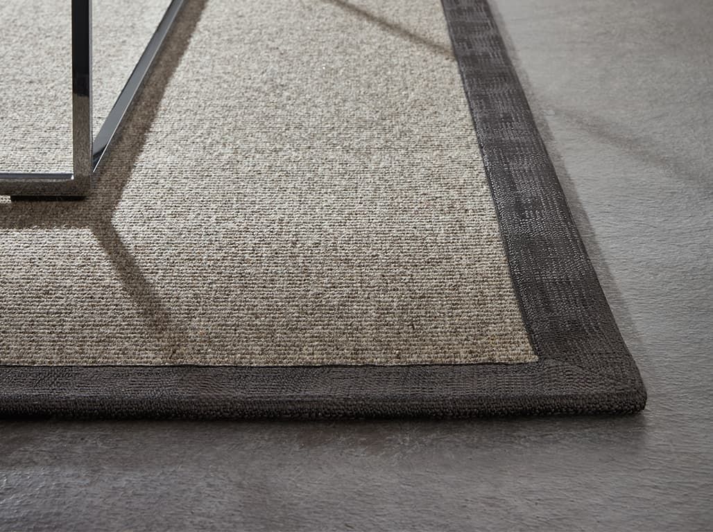 Nahaufnahme eines Teppichs mit dunklem Rand auf einem Betonboden.