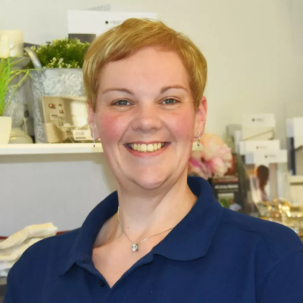 Eine Frau mit kurzen blonden Haaren lächelt und trägt ein blaues Hemd.