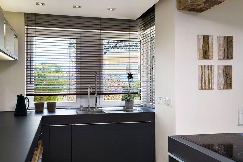 Küche mit dunkelgrauen Schränken, Spüle, Fenster mit Jalousien und dekorativer Wandgestaltung.