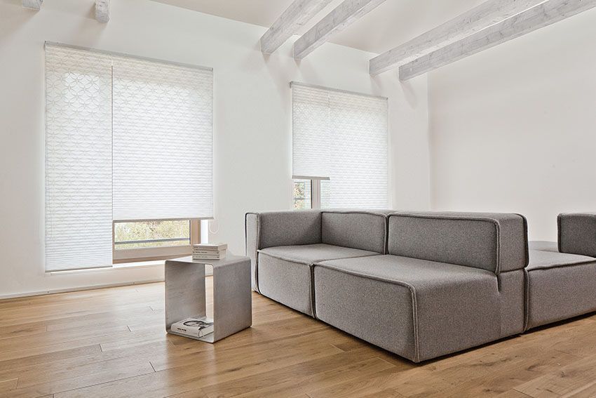 Modernes Wohnzimmer mit grauem Ecksofa, weißen Wänden und Holzboden.