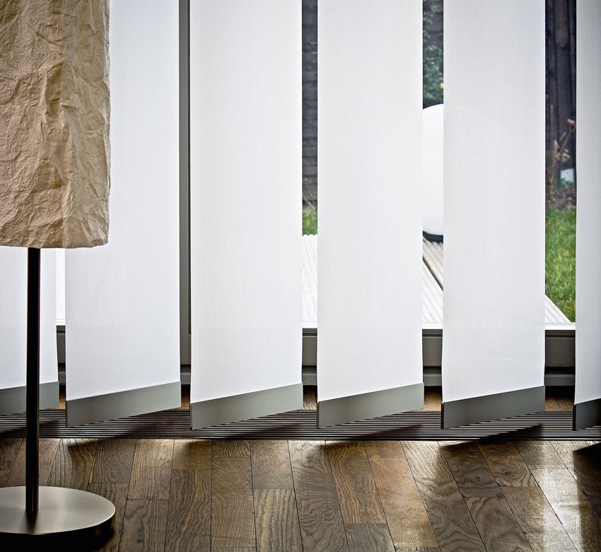 Weiße Vertikaljalousien, eine Lampe und ein Hartholzboden.