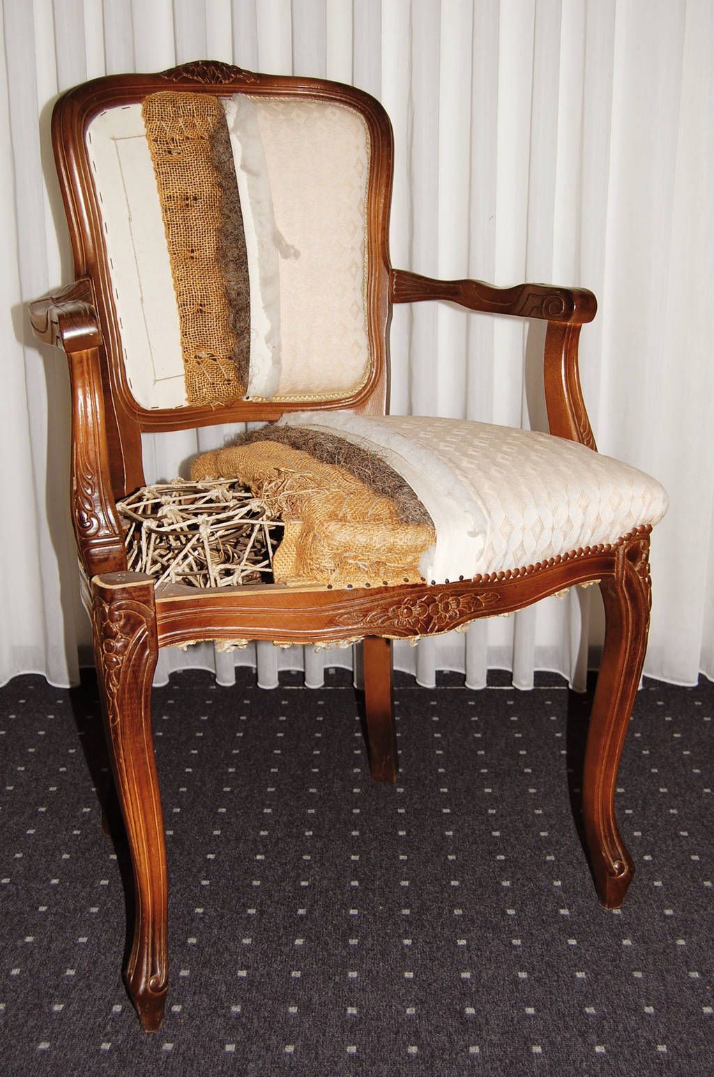 Stuhl mit sichtbaren Polsterschichten, reich verziertem Holzrahmen.