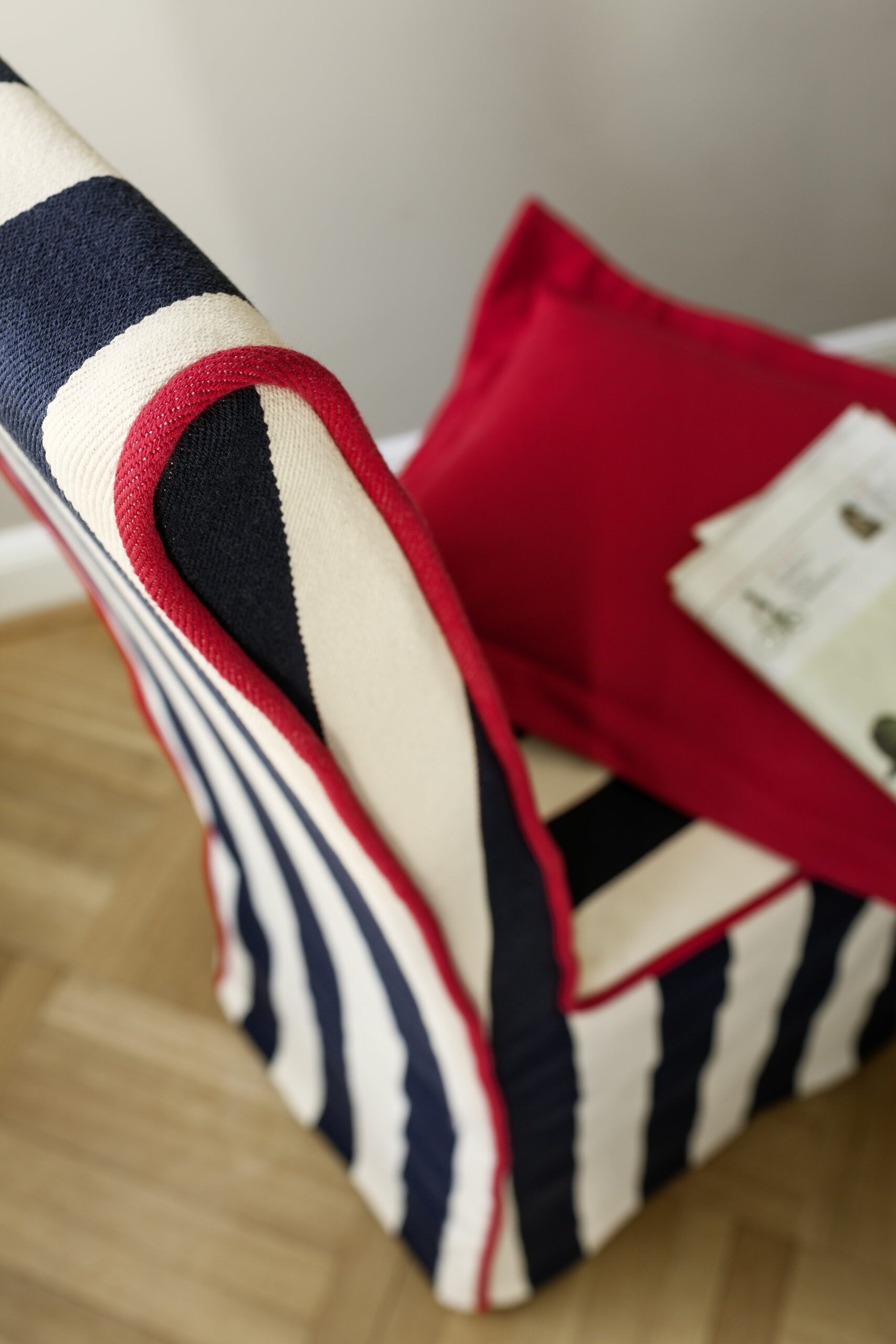 Nahaufnahme eines gestreiften Sessels mit rotem Kissen. Farben: Weiß, Marineblau und Rot.