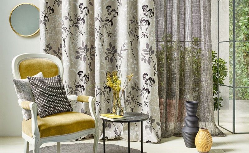 Wohnzimmer mit gemusterten Vorhängen, gelbem Sessel, Beistelltisch und dekorativen Vasen.