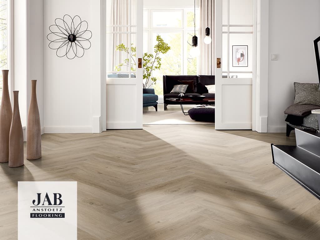 Fischgrätparkett in einem hellen Raum mit offener Tür.