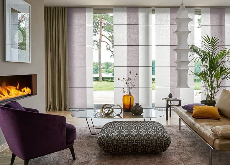 Wohnzimmer mit Kamin, lila Sessel, modernen Jalousien mit weißen und lila Streifen und großem Fenster.