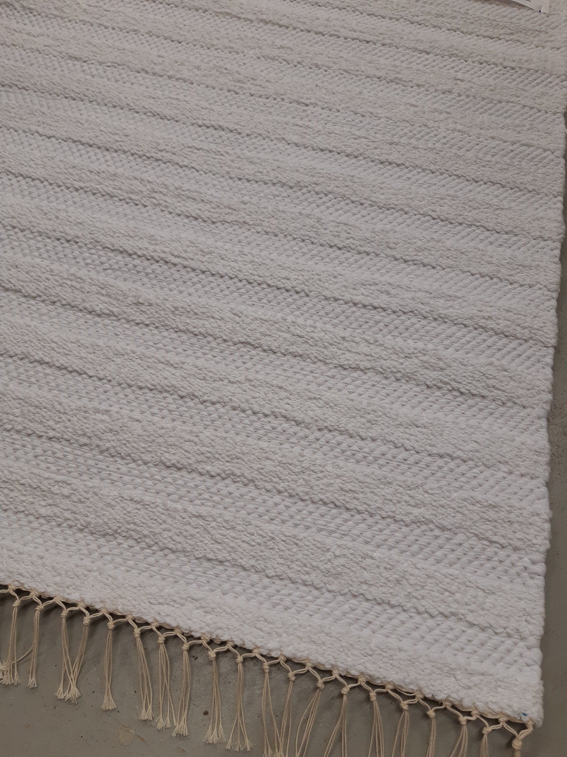 Valkoinen hapsuinen matto on betonilattialla.