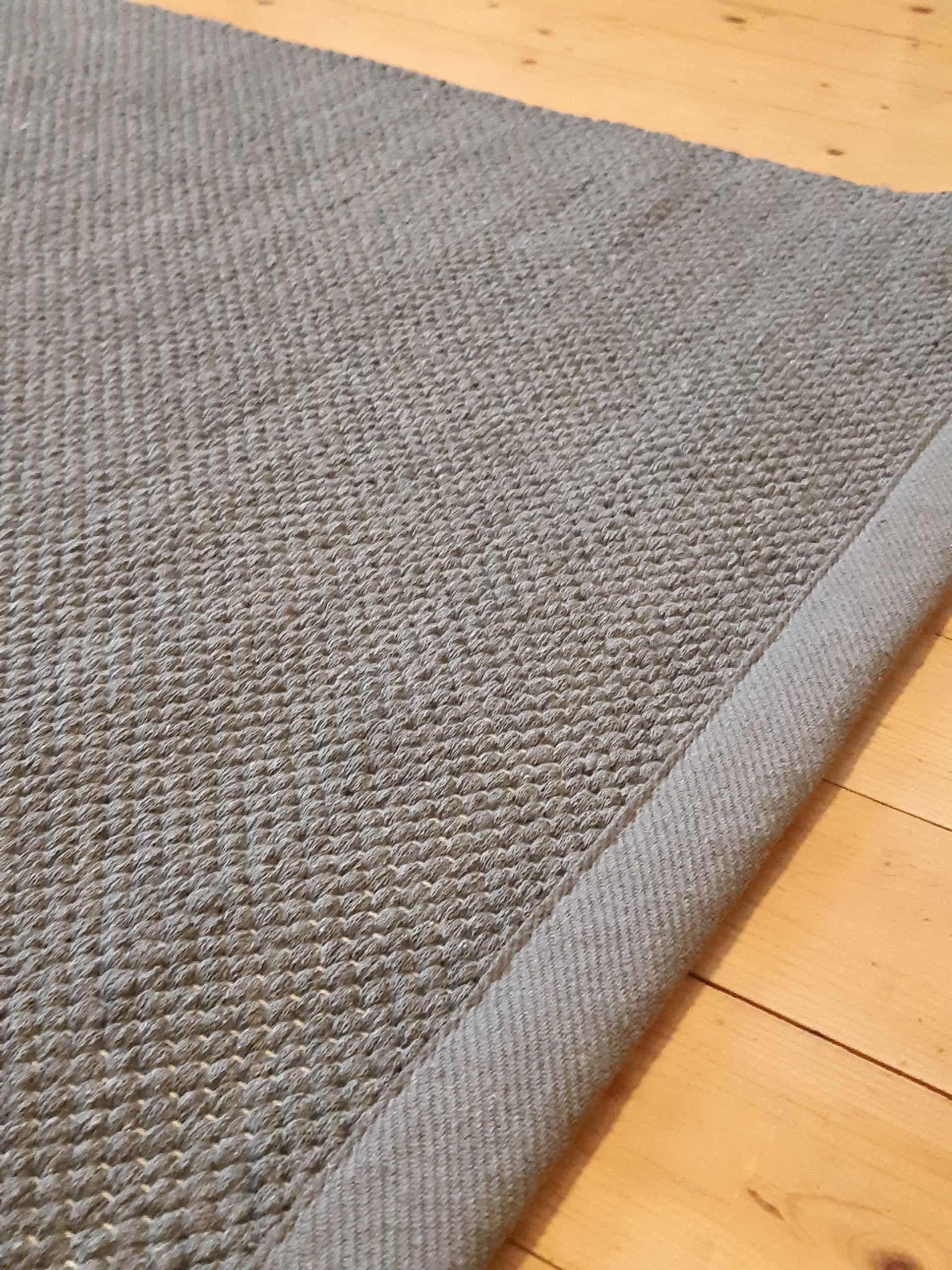 Lähikuva harmaasta matosta puulattialla