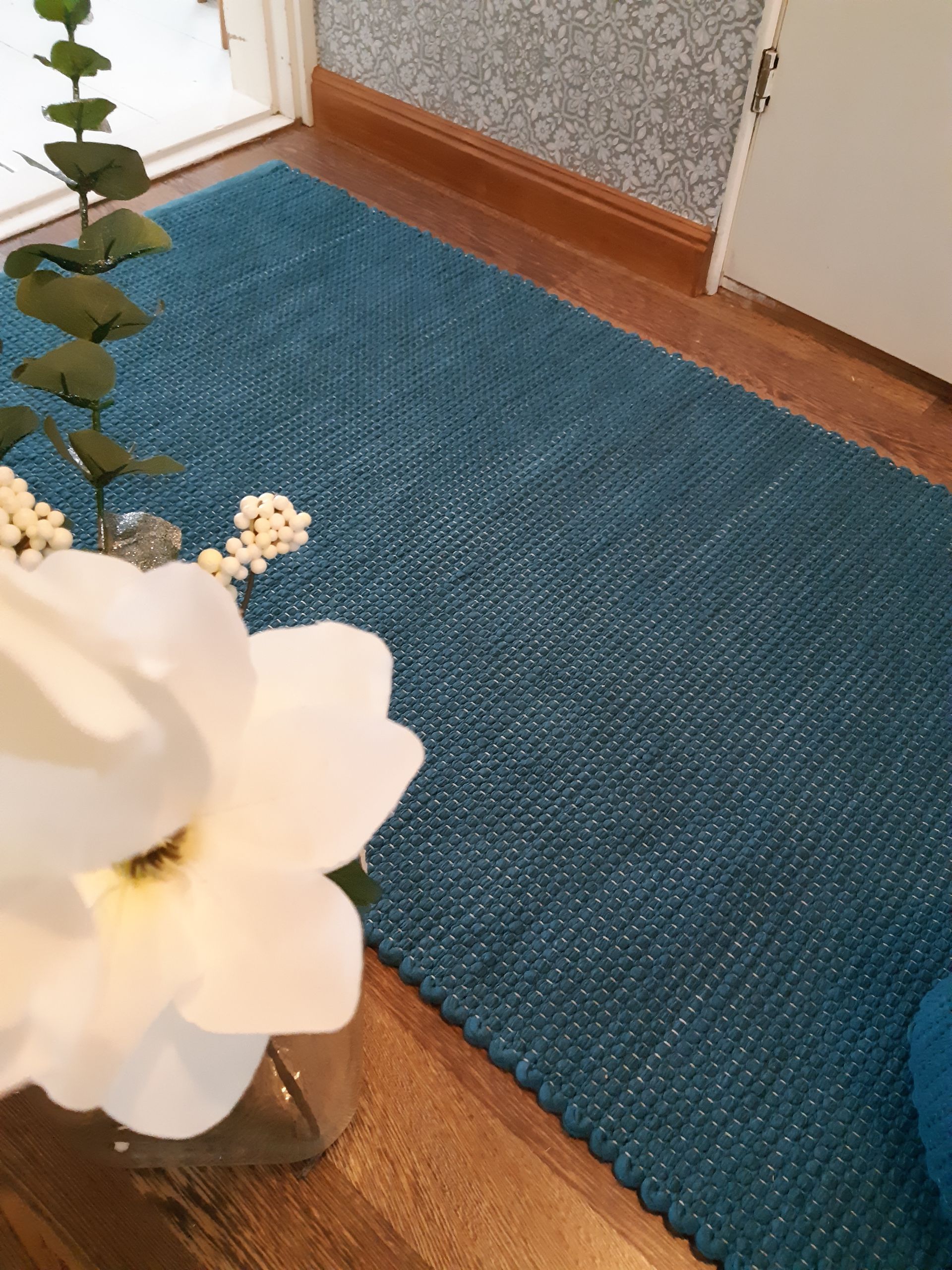 Sininen matto on puulattialla kukkamaljakon vieressä