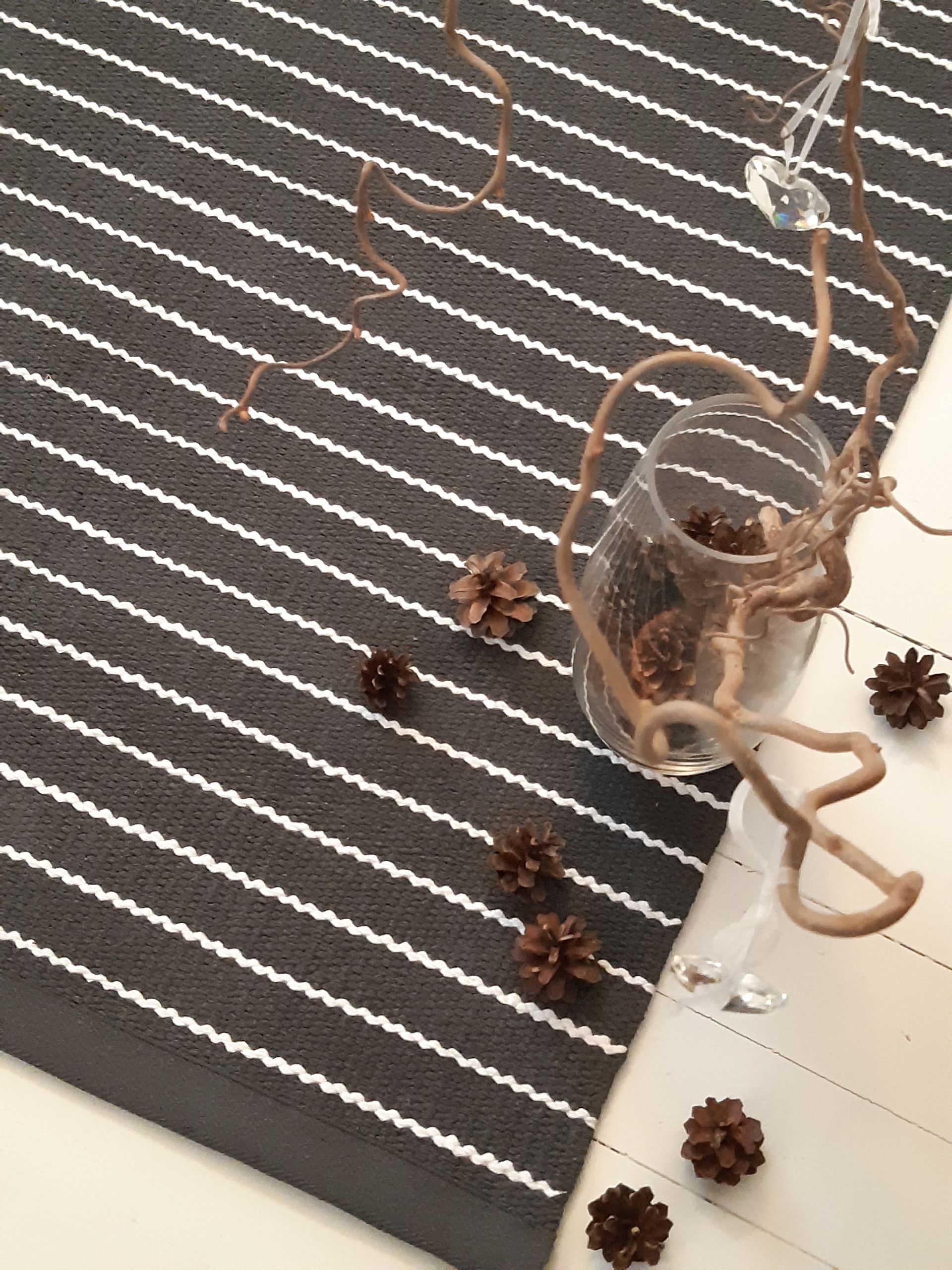 Mustavalkoinen raidallinen matto, jossa on käpyjä ja viinilasi
