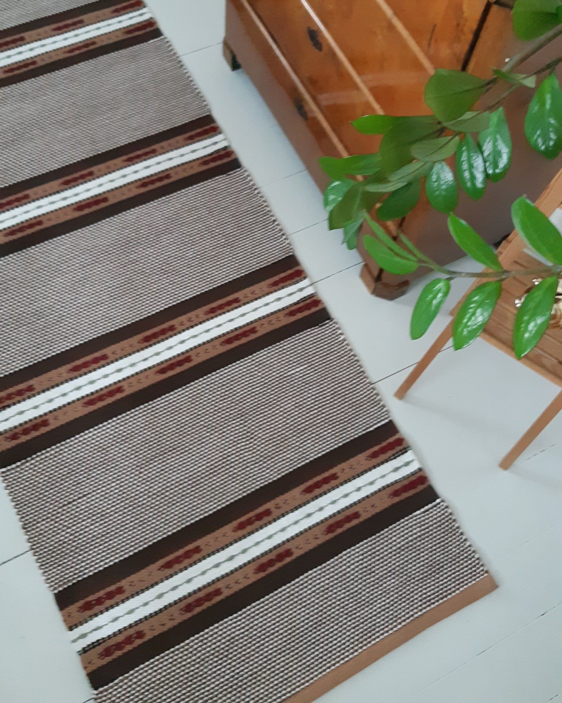 Ruskeavalkoinen raidallinen matto on lattialla kasvin vieressä