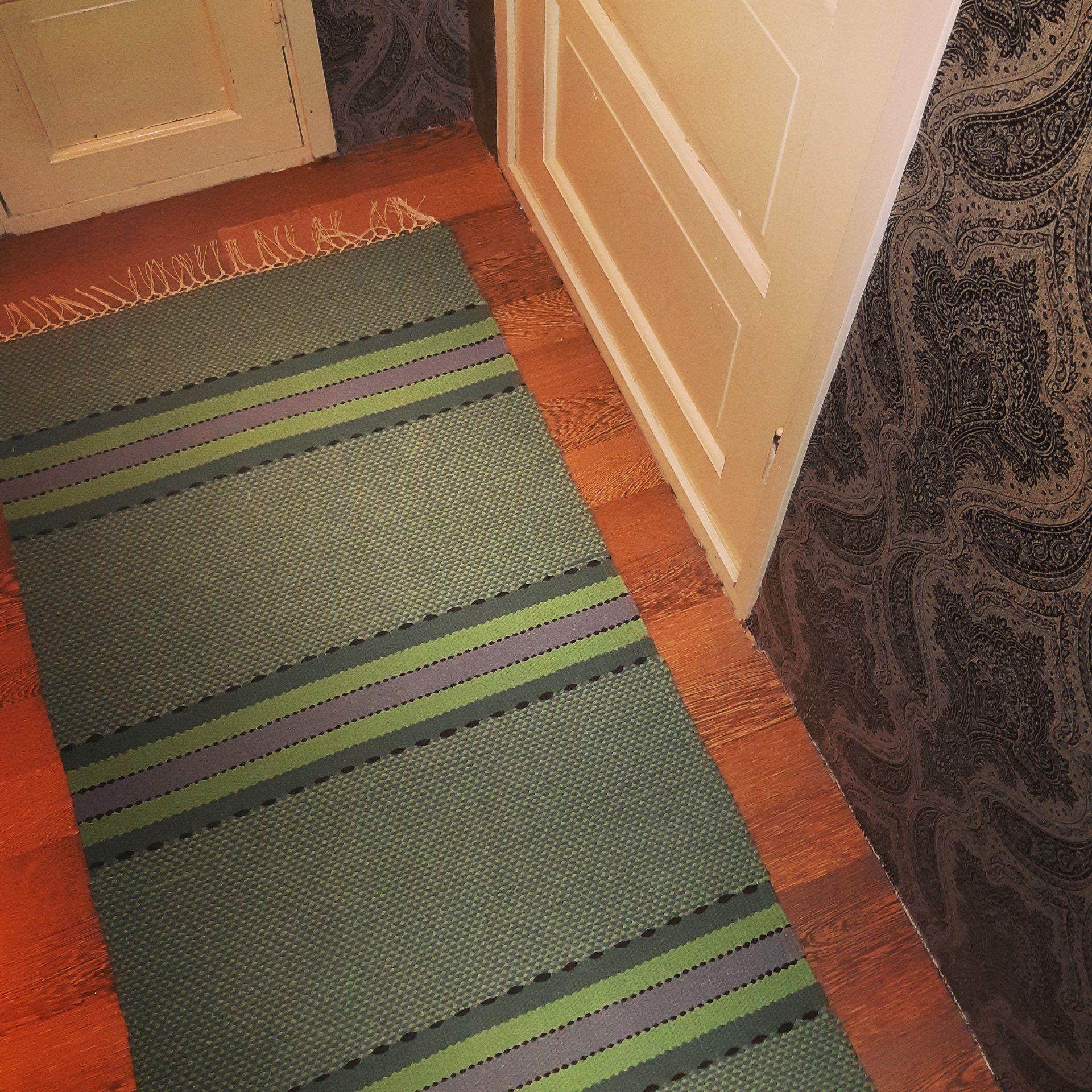 Lattialla oven vieressä on vihreä ja violetti matto