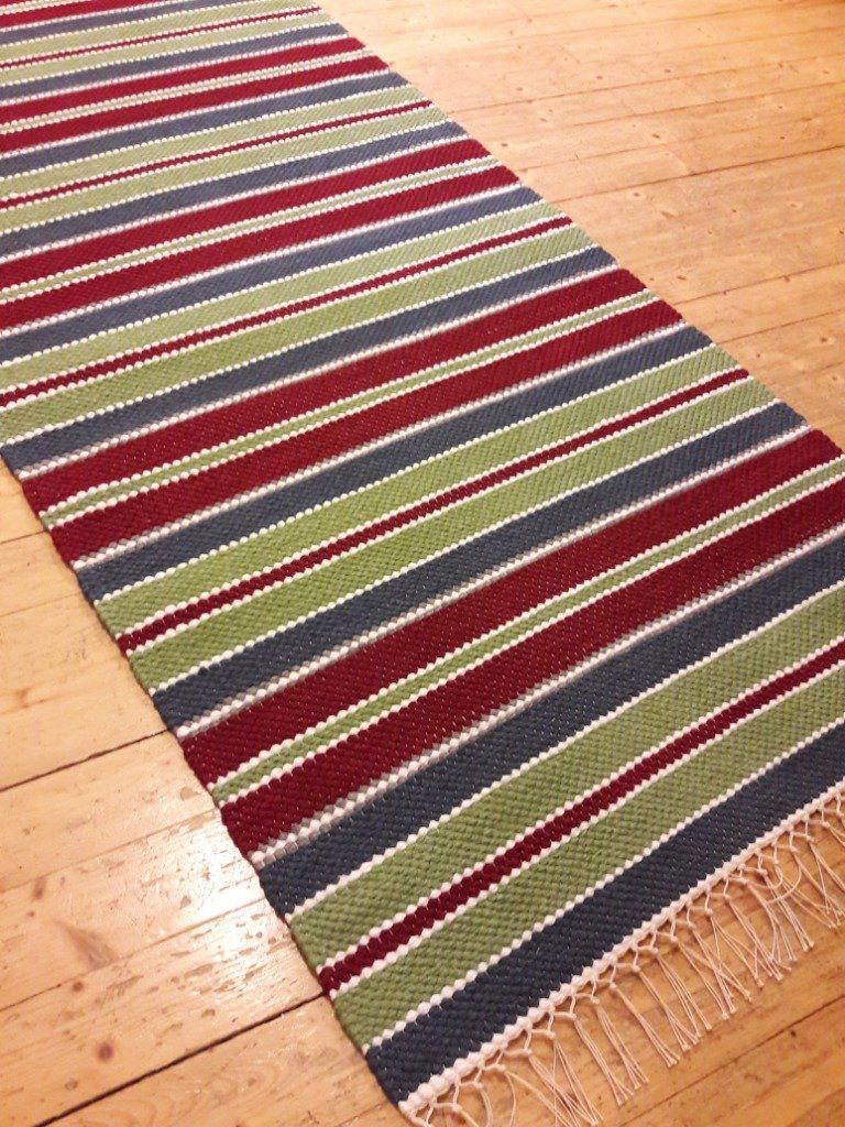 Punavihreä ja sininen raidallinen matto puulattialla