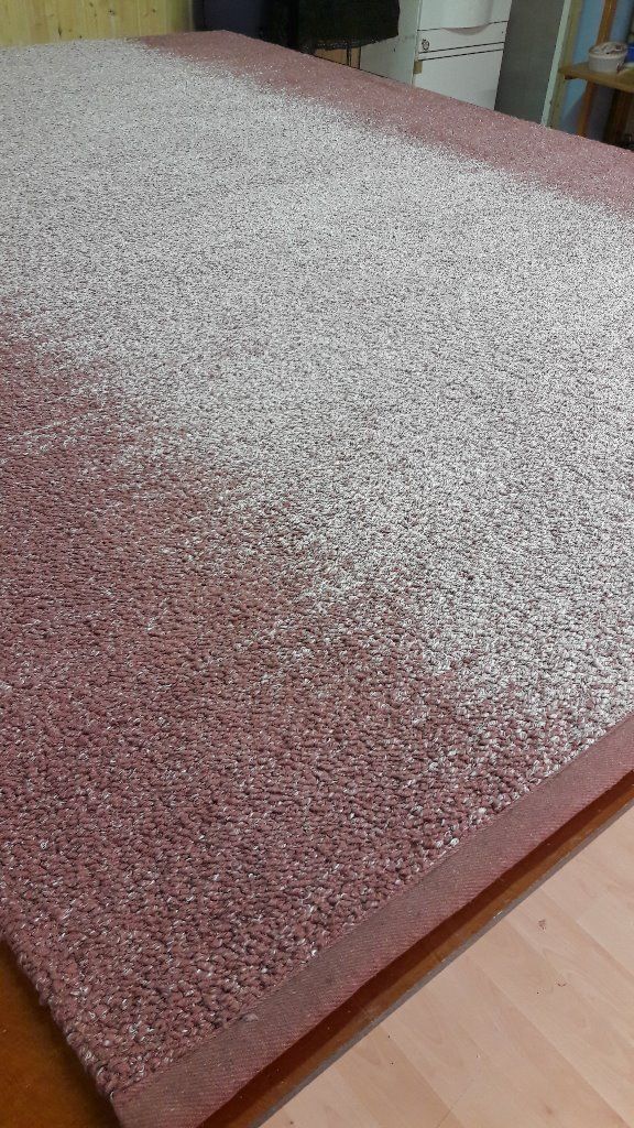 Vaaleanpunainen ja valkoinen matto on puulattialla.