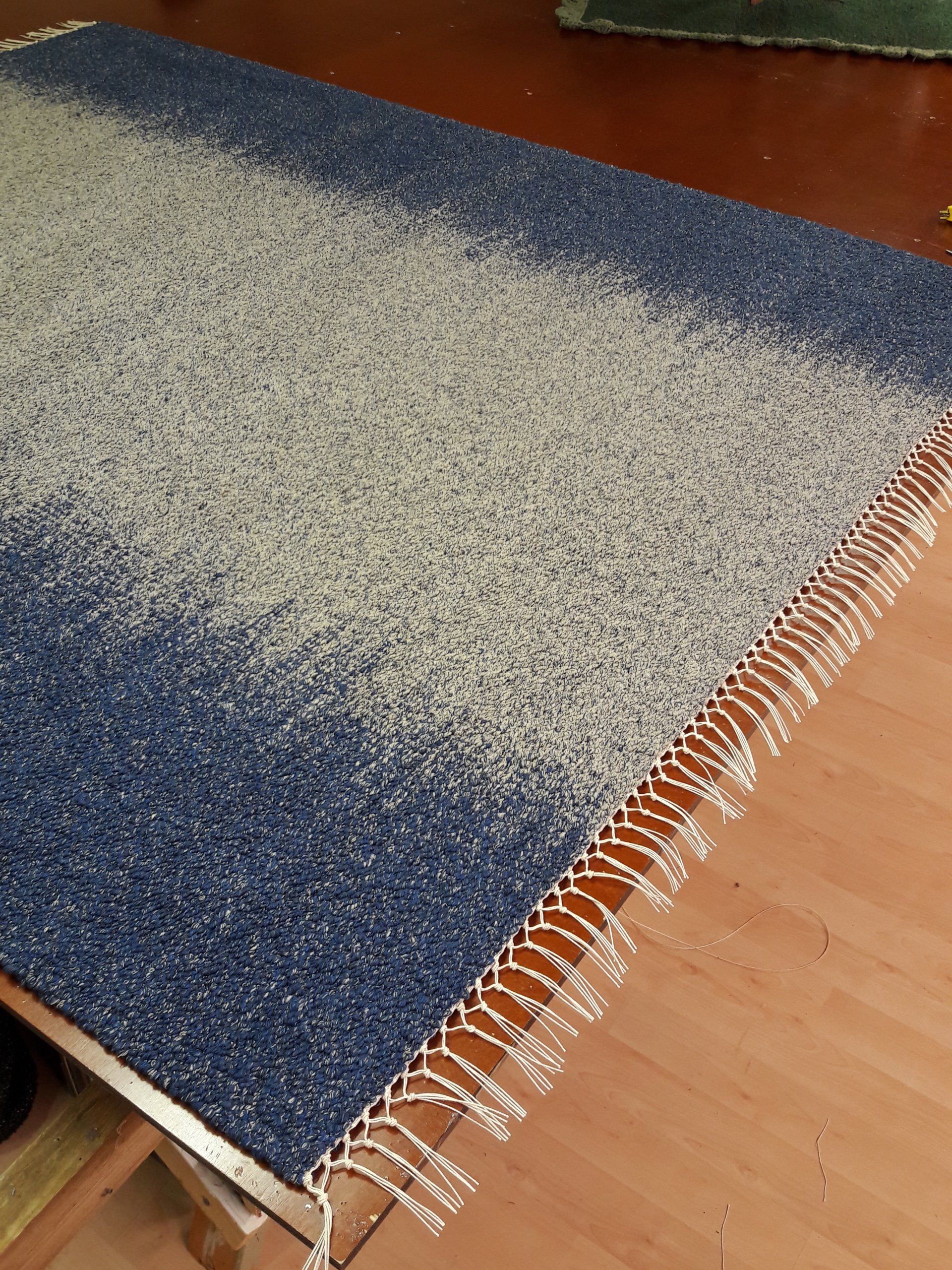 Sininen ja valkoinen hapsuinen matto on puulattialla