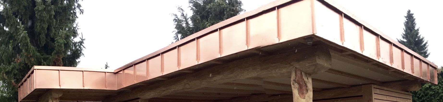 Eine Ansicht aus der Froschperspektive auf ein Gebäude mit einer neuen, polierten Kupferdachfassade vor dem Hintergrund von Bäumen.