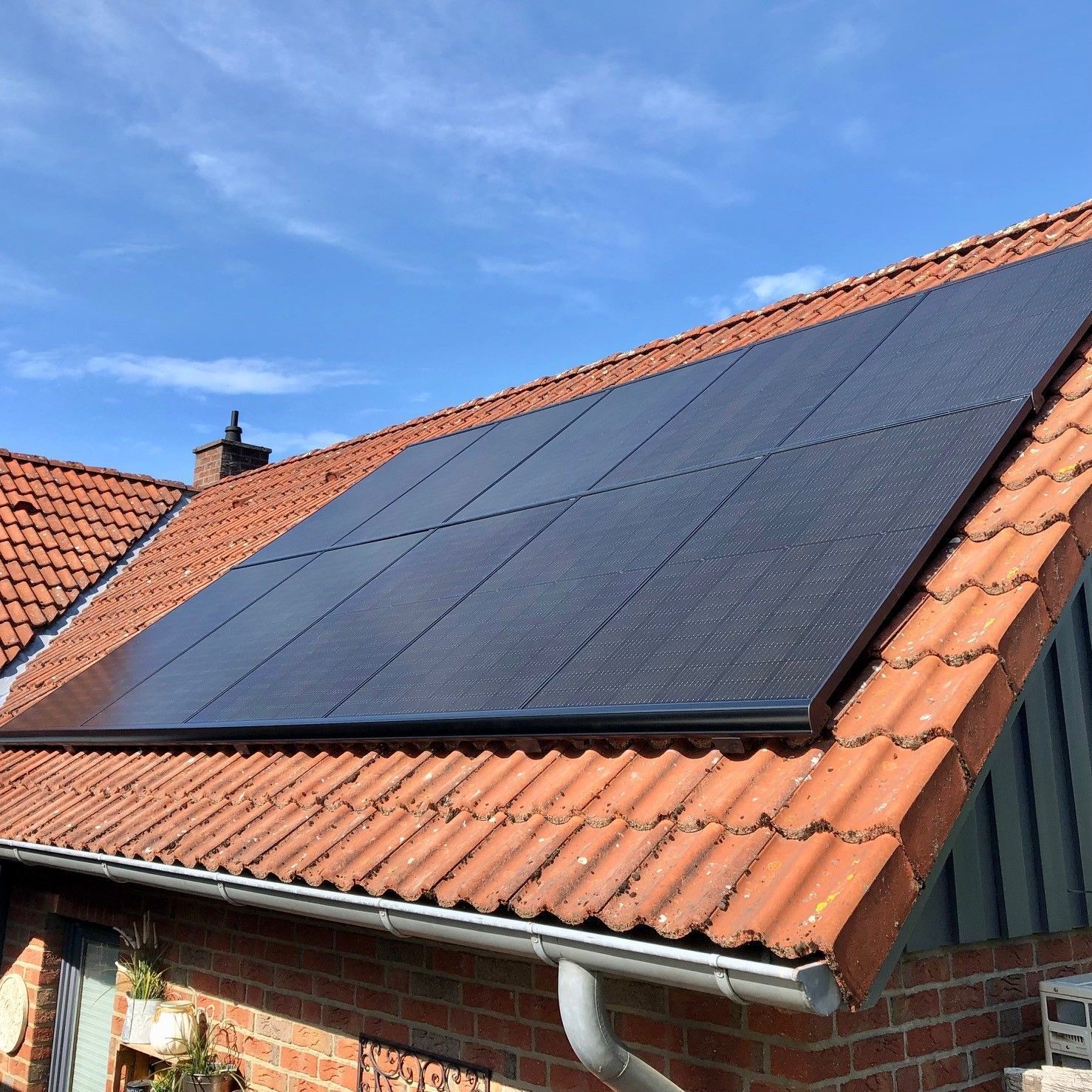 Ein Wohnhausdach mit Terrakotta-Ziegeln, auf dem unter einem klaren blauen Himmel eine rechteckige Anordnung schwarzer Solarpaneele zu sehen ist.