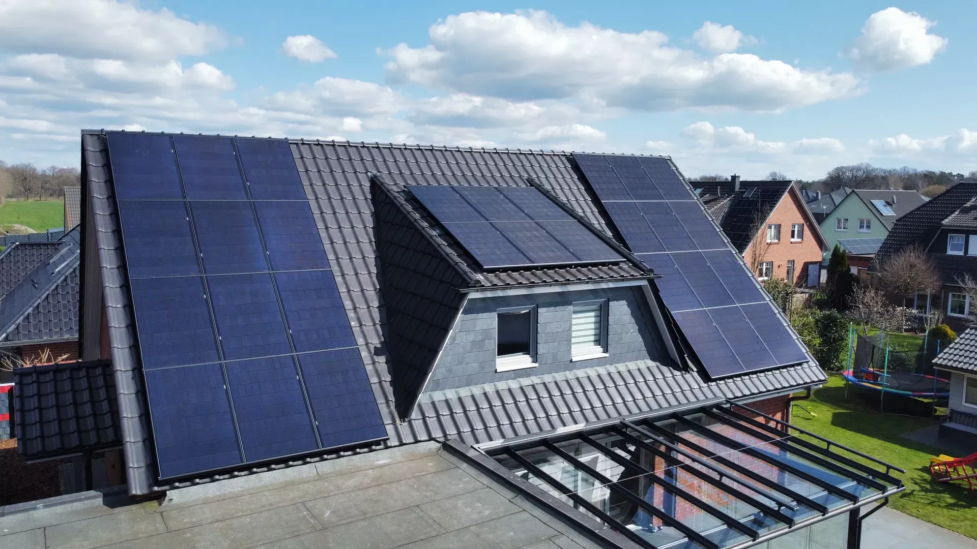 Ein Wohnhausdach mit dunklen Solarpaneelen, die über mehrere Dachflächen verteilt sind, und einem Dachgaubenfenster.