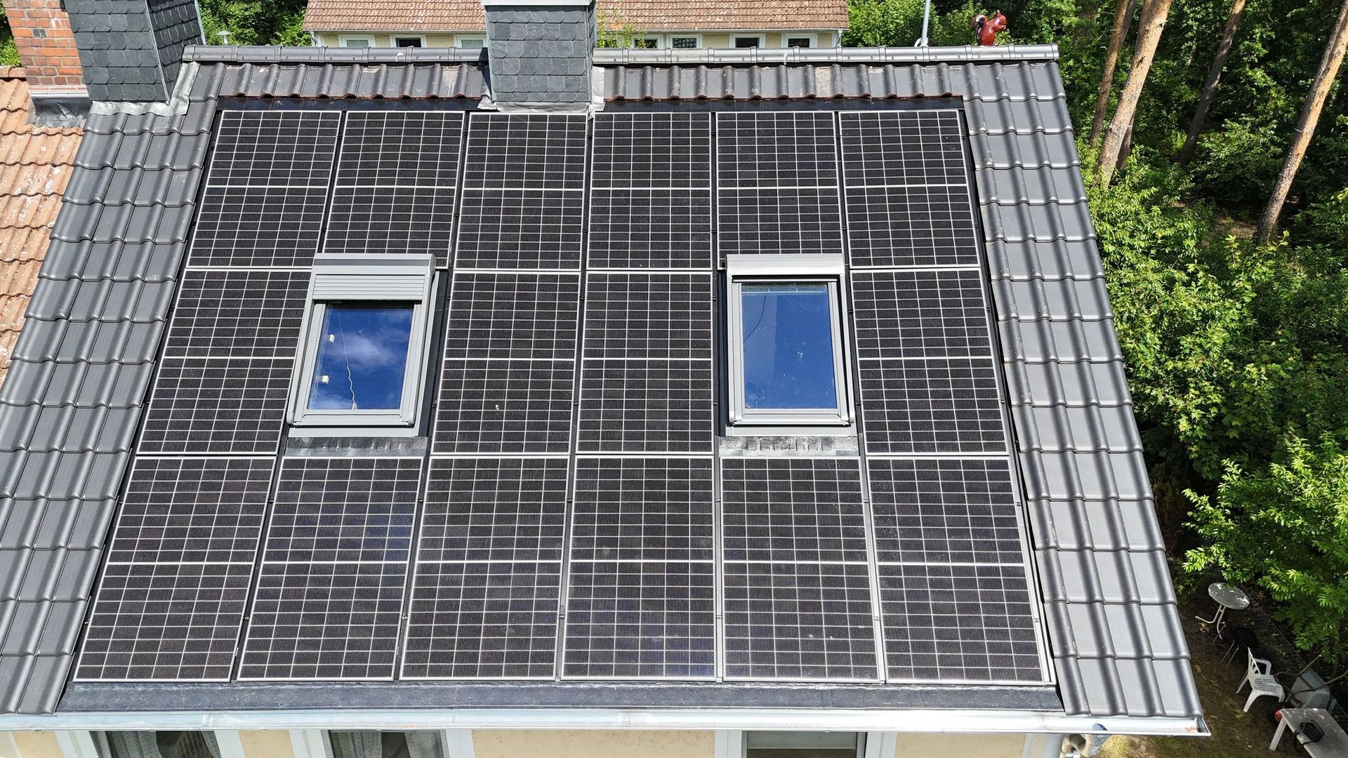 Ein Wohnhausdach mit integrierten Solardachziegeln und zwei Oberlichtern, die von dunklen, herkömmlichen Dachziegeln umgeben sind.