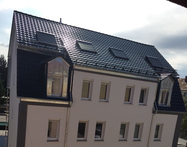 Wohnhaus mit mehreren Dachfenstern und Außenrollos auf neu gedecktem Dach.