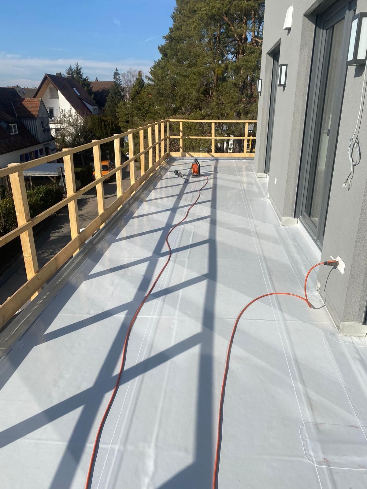 Großer Balkon mit Holzgeländer und heller Bodenabdichtung am Wohnhaus.