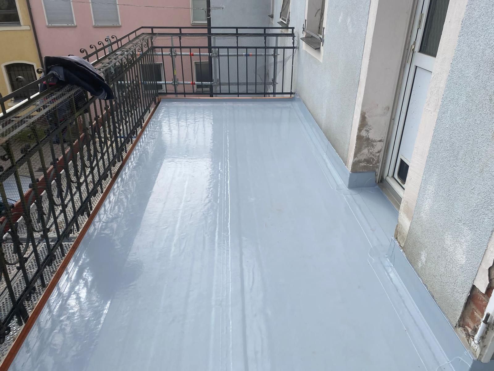 Balkon mit heller Bodenabdichtung und schwarzem Metallgeländer.