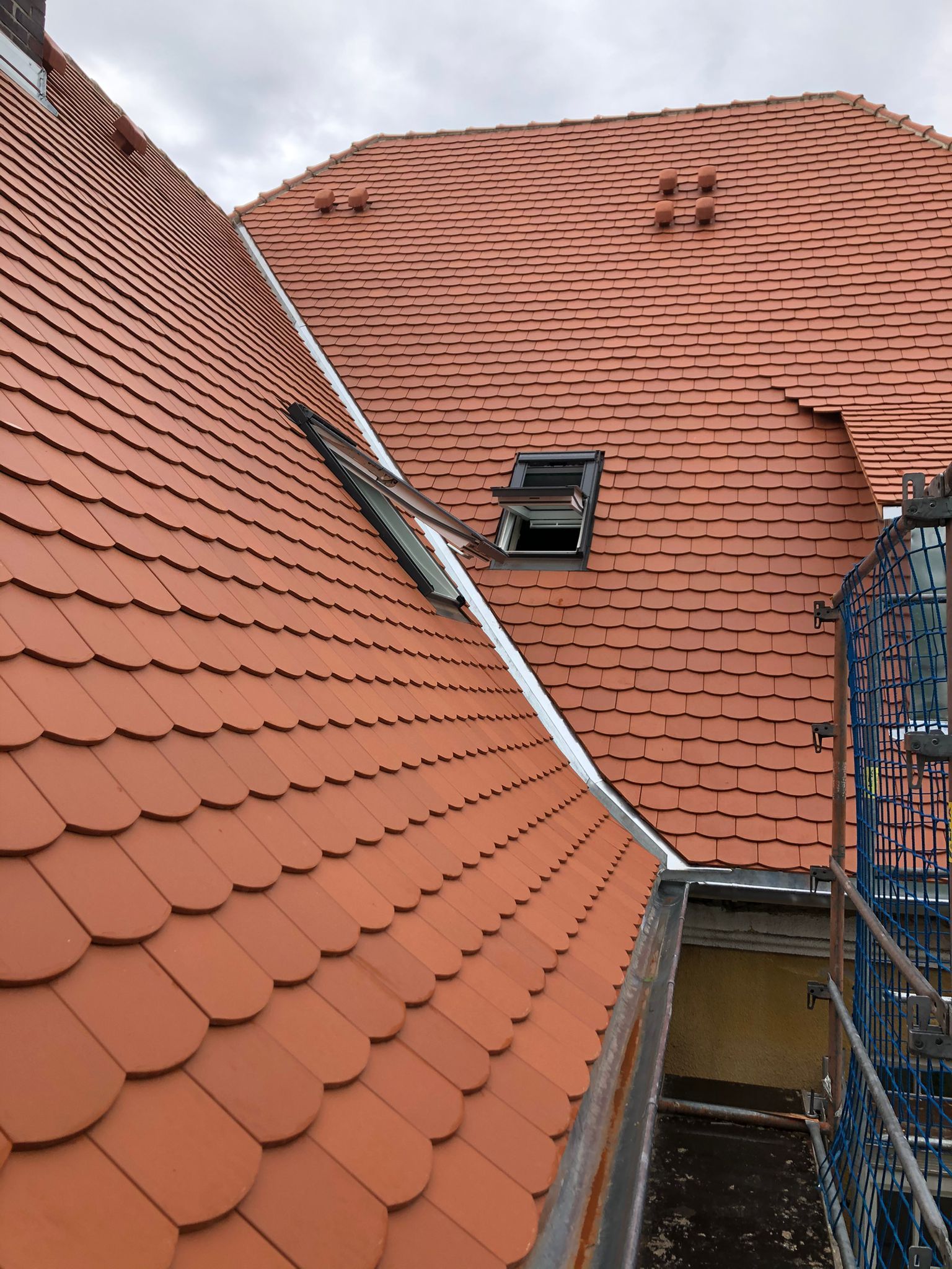 Großes Steildach mit roten Dachziegeln und integriertem Dachfenster unter bewölktem Himmel