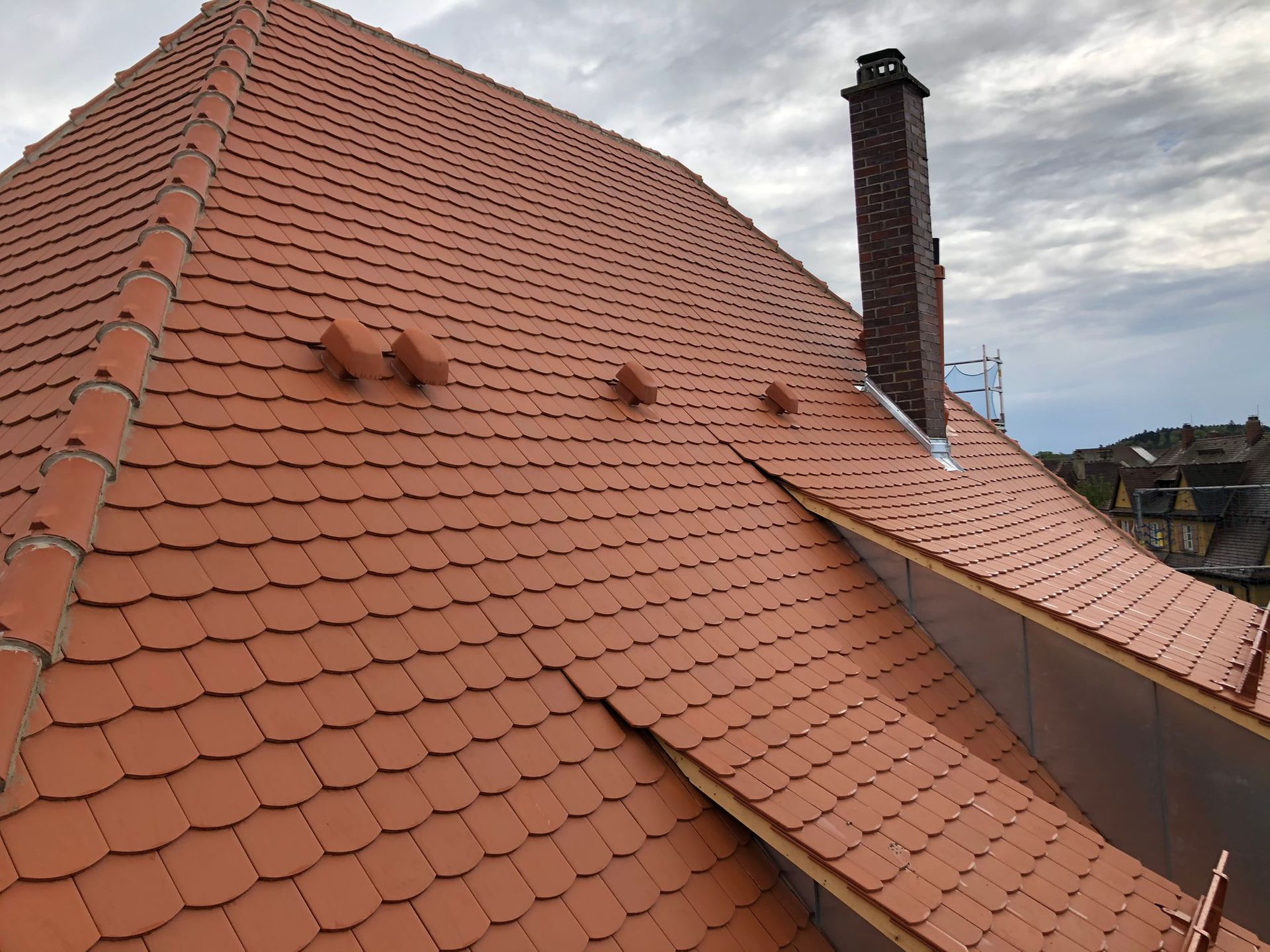Steildach mit roten Biberschwanzziegeln und gemauertem Schornstein unter bewölktem Himmel