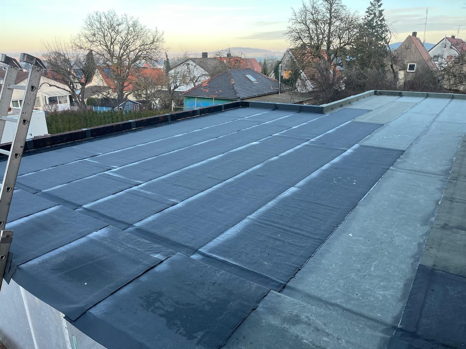 Großes Flachdach mit dunkler Bitumenabdichtung in parallel verlegten Bahnen, mit sichtbaren Nähten und leichtem Gefälle